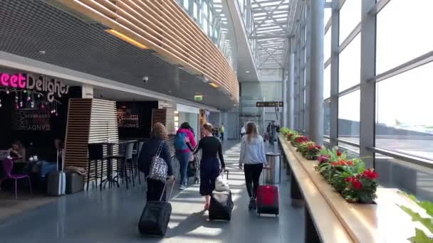 Латвия, Рига, 23 апреля 2019 года: Пассажиры с чемоданами и тележками в аэропорту, входят на посадку в самолет, окна с видом на поле аэропорта, глянцевый пол, люди с ручной клади — стоковое видео