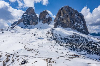Dolomitlerin güneşli bir günde İtalya 'daki karla kaplı dağların havadan görünüşü, Canazei, insansız hava aracı bakış açısı, çarpık yol, beyaz bulutlu mavi gökyüzü, dünyada ünlü bir yer, UNESCO anıtı.