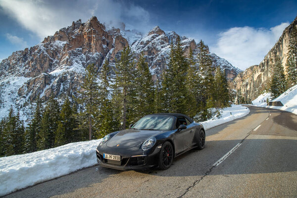 Italy, The Dolomites, Canazei, 1 May 2019: The expensive sports cars a stops on the twisted road against snow-covered mountains Dolomites, Porsche 911 Turbo 4 GTS, monument UNESCO, sunny weather