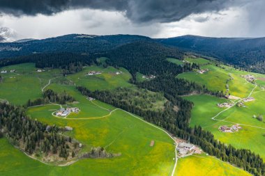 Olağandışı yeşil İtalyan Alpleri çayırları, dağların yeşil yamaçları, Bolzano, vadideki devasa bulutlar, evlerin çatıları, arka planda Dolomitler, bulutların arasından gün ışığı.