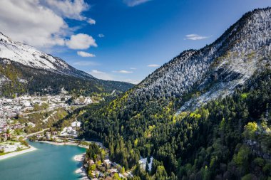 Molveno, İtalya 'nın Olasılıkdışı hava manzarası, göl mavisi suyu, boş kumsal, arka planda karla kaplı dağlar Dolomitler, dağ evinin çatısı, güneşli hava, rıhtım,, 