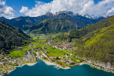 Molveno, İtalya 'nın Olasılıkdışı hava manzarası, göl mavisi suyu, boş kumsal, arka planda karla kaplı dağlar Dolomitler, dağ evinin çatısı, güneşli hava, rıhtım,, 