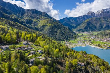 Molveno, İtalya 'nın Olasılıkdışı hava manzarası, göl mavisi suyu, boş kumsal, arka planda karla kaplı dağlar Dolomitler, dağ evinin çatısı, güneşli hava, rıhtım,, 
