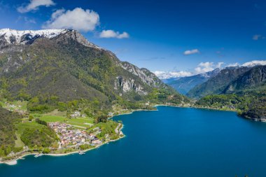 Molveno, İtalya 'nın Olasılıkdışı hava manzarası, göl mavisi suyu, boş kumsal, arka planda karla kaplı dağlar Dolomitler, dağ evinin çatısı, güneşli hava, rıhtım,, 