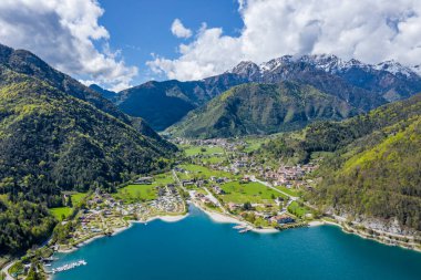 Molveno, İtalya 'nın Olasılıkdışı hava manzarası, göl mavisi suyu, boş kumsal, arka planda karla kaplı dağlar Dolomitler, dağ evinin çatısı, güneşli hava, rıhtım,, 