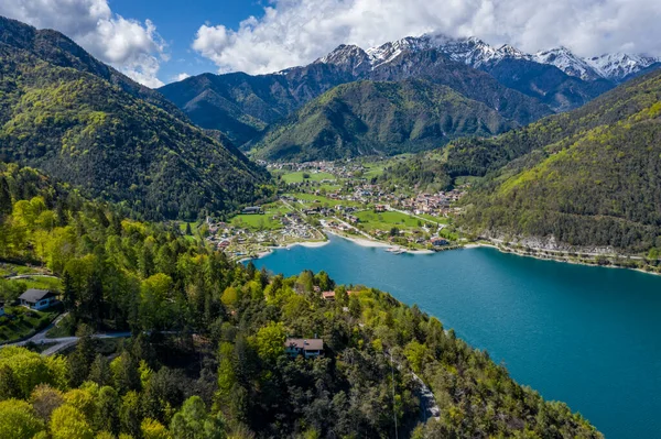 Molveno, İtalya 'nın Olasılıkdışı hava manzarası, göl mavisi suyu, boş kumsal, arka planda karla kaplı dağlar Dolomitler, dağ evinin çatısı, güneşli hava, rıhtım,, 