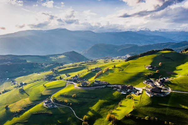 Вид с воздуха на невероятные зеленые луга итальянских Альп, зеленые склоны гор, Больцано, огромные облака над долиной, крыши домов, Доломиты на заднем плане, солнечные лучи сквозь облака — стоковое фото