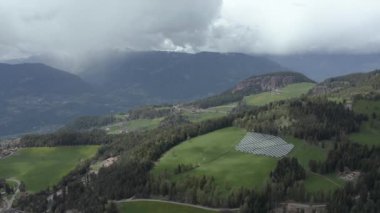 İtalya 'nın yeşil yamaçlarındaki güneş pillerinin hava manzarası Trentino, vadideki dev bulutlar, yerleşim yerlerinin çatıları, yeşil çayırlar, temiz bir enerji, güneşin enerjisi.