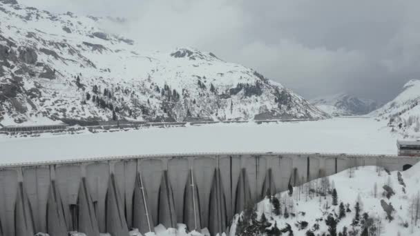 Flygvideo från drönare som flyger över en snötäckt damm i södra delen av Österrike eller norra Italien, Trentino, grupp av svarta sportbilar går på en damm, är väg längs sjön och bergen — Stockvideo