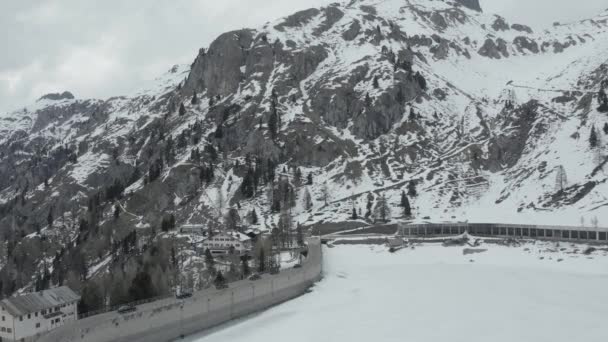 Flygvideo från drönare som flyger över en snötäckt damm i södra delen av Österrike eller norra Italien, Trentino, grupp av svarta sportbilar går på en damm, är väg längs sjön och bergen — Stockvideo