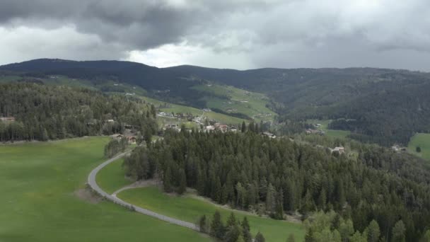 Widok z lotu ptaka na nieprawdopodobne zielone łąki Alp Włoskich, zielone zbocza gór, Bolzano, ogromne chmury nad doliną, dachy domów, Dolomity na tle, promienie słońca przez chmury — Wideo stockowe