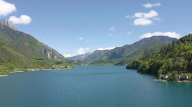 Molveno, İtalya 'nın Olasılıkdışı hava manzarası, İHA' lar gölün masmavi suları üzerinde alçaktan uçuyor, boş bir plaj, arka planda dağ yamaçları, güneşli hava, kıyı şeridi.