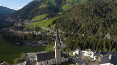 Gün batımında kilisesi olan vadi manzarası, İtalya, Trentino, Güney Tyrol dağlarının yeşil yamaçları, yeşil çayırlar, arka planda Dolomitler, insansız hava aracı uçuşları.