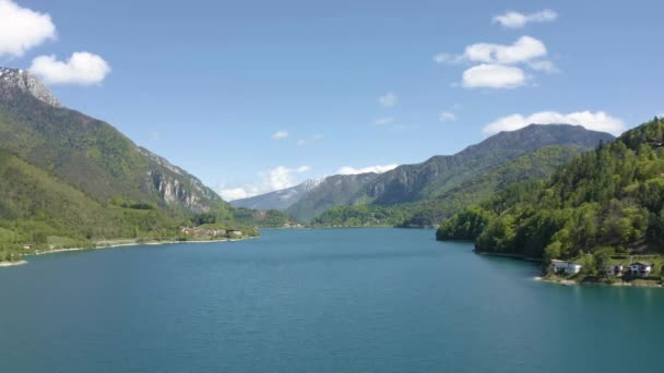 A paisagem aérea improvável da aldeia Molveno, Itália, drone voa baixo sobre a água azul do lago, uma praia vazia, encostas cobertas de neve de montanha no fundo, tempo ensolarado, costa — Vídeo de Stock