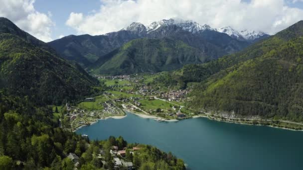 Nieprawdopodobny powietrzny krajobraz wsi Molveno, Włochy, lazurowa woda jeziora, pusta plaża, pokryte śniegiem góry Dolomity na tle, dach domku letniskowego, słoneczna pogoda, molo, wybrzeże, — Wideo stockowe