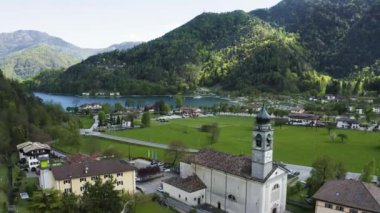 Molveno 'nun Olasılıkdışı hava manzarası, İtalya' nın Trentino-Alto Adige bölgesinde, San Carlo Borromeo kilisesi, güneşli hava, bir rıhtım ve kıyı şeridi.,