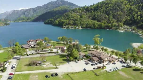 The Improbable aerial landscape of village Molveno, Italy, azure water of lake, empty beach, snow covered mountains Dolomites on background, roof top of chalet, sunny weather, a piers, coastline, — Stock Video