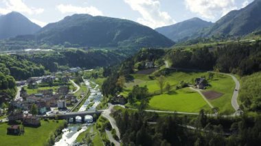 Vadi manzarası Cares, Trentino, İtalya 'nın yeşil yamaçları, vadinin üzerindeki dev bulutlar, evlerin çatıları, arka plandaki Dolomitler, köprüler, nehir ve yollar, bahar renkleri.