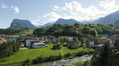 Vadi manzarası Cares, Trentino, İtalya 'nın yeşil yamaçları, vadinin üzerindeki dev bulutlar, evlerin çatıları, arka plandaki Dolomitler, köprüler, nehir ve yollar, bahar renkleri.