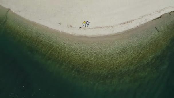 O casal senta-se em uma praia, água azul do lago, A paisagem aérea improvável, Itália, Dolomites, tempo ensolarado, litoral — Vídeo de Stock