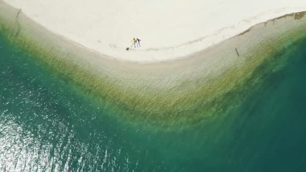 The couple sits on a beach, azure water of lake, the improbable aerial landscape, Italy, Dolomites, sunny weather, coastline — Stock Video