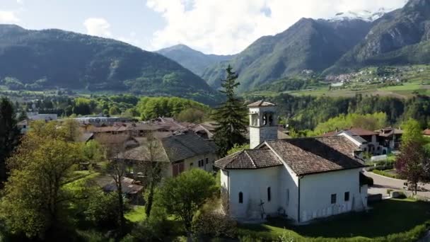 ケア、トレンティーノ、イタリアの山の緑の斜面、谷の上の巨大な雲、家の屋根の上、背景にドロマイトで教会と谷の空中ビュー — ストック動画