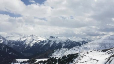 İtalya, Dolomitler, Canazei, Dağların üzerinde süzülen uçan dron, arka planda karla kaplı dağlar, kıvrımlı yol, mavi gökyüzü beyaz bulutlar, güneşli hava, hiç kimse