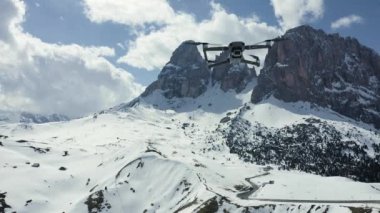 İtalya, Dolomitler, Canazei, 10 Mayıs 2019: Uçan dron, arka planda karla kaplı dağlar, kıvrımlı yollar, beyaz bulutlu mavi gökyüzü, güneşli hava