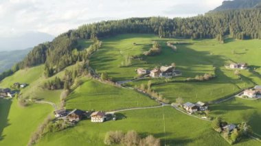 Olağandışı yeşil İtalyan Alpleri çayırları, dağların yeşil yamaçları, Bolzano, vadideki devasa bulutlar, evlerin çatıları, arka planda Dolomitler, bulutların arasından gün ışığı.