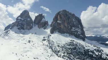 Dolomitlerin güneşli bir günde İtalya 'da karla kaplı dağların havadan görünüşü, Canazei, insansız hava aracı bakış açısı, kıvrımlı yol, beyaz bulutlu mavi gökyüzü, dünyada ünlü bir yer, UNESCO anıtı.