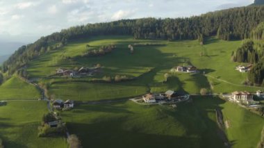 Olağandışı yeşil İtalyan Alpleri çayırları, dağların yeşil yamaçları, Bolzano, vadideki devasa bulutlar, evlerin çatıları, arka planda Dolomitler, bulutların arasından gün ışığı.
