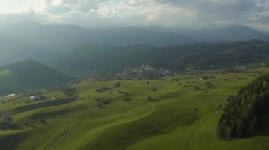 Olağandışı yeşil İtalyan Alpleri çayırları, dağların yeşil yamaçları, Bolzano, vadideki devasa bulutlar, evlerin çatıları, arka planda Dolomitler, bulutların arasından gün ışığı.