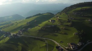 Olağandışı yeşil İtalyan Alpleri çayırları, dağların yeşil yamaçları, Bolzano, vadideki devasa bulutlar, evlerin çatıları, arka planda Dolomitler, bulutların arasından gün ışığı.