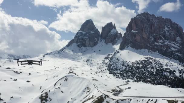 Italien, Dolomiterna, Canazei, 10 maj 2019: Den flygande drönaren hängde över berg, på en bakgrund snötäckta berg, den slingrande vägen, den blå himlen med vita moln, soligt väder — Stockvideo