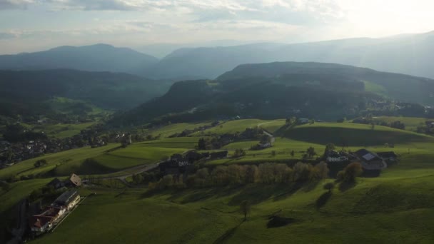 Widok z lotu ptaka na nieprawdopodobne zielone łąki Alp Włoskich, zielone zbocza gór, Bolzano, ogromne chmury nad doliną, dachy domów, Dolomity na tle, promienie słońca przez chmury — Wideo stockowe