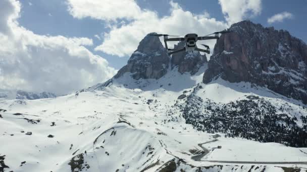 Italia, Dolomiti, Canazei, 10 maggio 2019: Il drone volante sospeso sulle montagne, su uno sfondo innevato, la strada tortuosa, il cielo blu con nuvole bianche, il tempo soleggiato — Video Stock