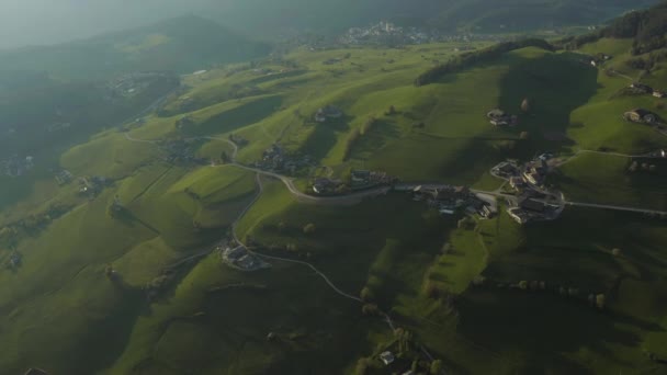 Widok z lotu ptaka na nieprawdopodobne zielone łąki Alp Włoskich, zielone zbocza gór, Bolzano, ogromne chmury nad doliną, dachy domów, Dolomity na tle, promienie słońca przez chmury — Wideo stockowe