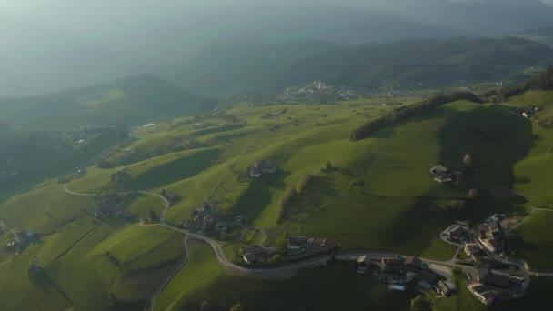 Vista aérea de prados verdes improváveis de Alpes italianos, encostas verdes das montanhas, Bolzano, nuvens enormes sobre um vale, topos de telhado de casas, Dolomites no fundo, raios de sol através de nuvens — Vídeo de Stock