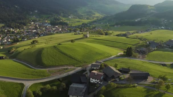 Pemandangan udara dari padang rumput hijau yang tidak memungkinkan dari Alpen Italia, lereng hijau dari pegunungan, Bolzano, awan besar di atas lembah, atap rumah, Dolomites di latar belakang, sinar matahari melalui awan — Stok Video