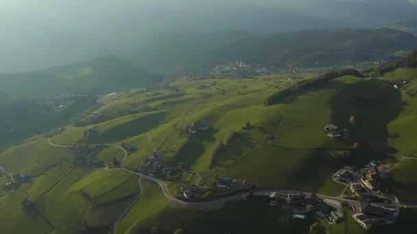 Вид с воздуха на невероятные зеленые луга итальянских Альп, зеленые склоны гор, Больцано, огромные облака над долиной, крыши домов, Доломиты на заднем плане, солнечные лучи сквозь облака — стоковое видео