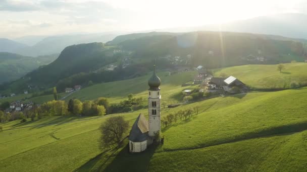 Flygfoto över pittoresk dal med kapell i Bolzano vid solnedgången, Trentino, fantastiska gröna ängar i bergen i Italien, tak toppar av hus, Dolomiter på bakgrunden, drönare flyger runt kapell — Stockvideo