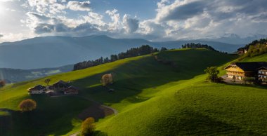 Aerial view of improbable green meadows of Italian Alps, green slopes of the mountains, Bolzano, huge clouds over a valley, roof tops of houses, Dolomites on background, sunshines through clouds clipart