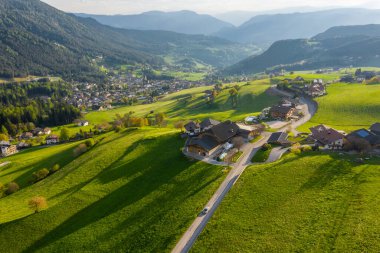 Olağandışı yeşil İtalyan Alpleri çayırları, dağların yeşil yamaçları, Bolzano, vadideki devasa bulutlar, evlerin çatıları, arka planda Dolomitler, bulutların arasından gün ışığı.