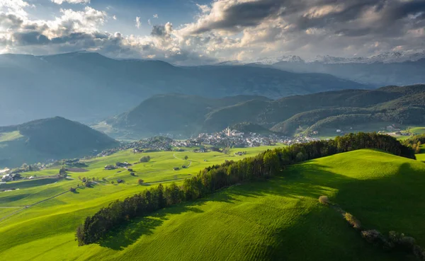 Aerial view of improbable green meadows of Italian Alps, green slopes of the mountains, Bolzano, huge clouds over a valley, roof tops of houses, Dolomites on background, sunshines through clouds — Stock Photo, Image