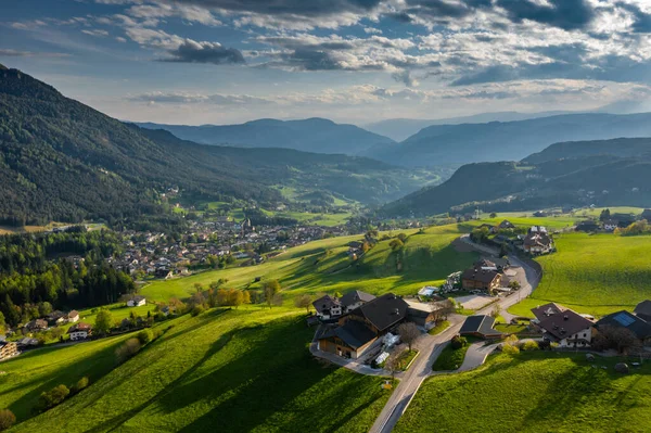 Aerial view of improbable green meadows of Italian Alps, green slopes of the mountains, Bolzano, huge clouds over a valley, roof tops of houses, Dolomites on background, sunshines through clouds — Stock Photo, Image