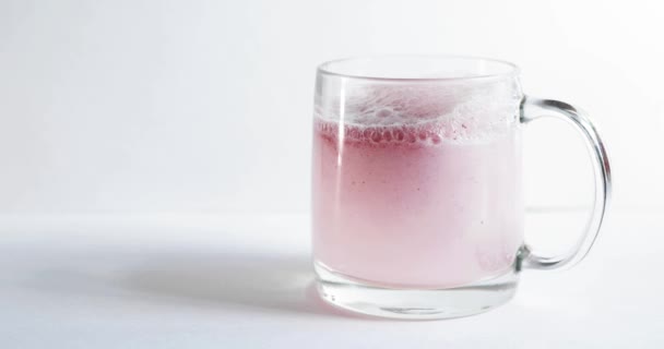 Comprimé mousseux jeté dans un verre transparent, le verre est sur un fond blanc, une pilule pour le froid de couleur claret, des bulles se lèvent, éclaboussures décollent d'un verre — Video