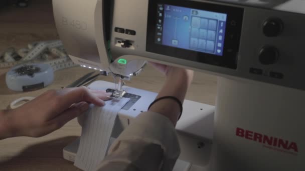 Rusia, San Petersburgo, 01 de marzo de 2019: La niña se sienta en la máquina de coser automática de Bernina en el estudio de costura y cose cualquier ropa, pantalla led, temas para el trabajo, iluminación local — Vídeos de Stock