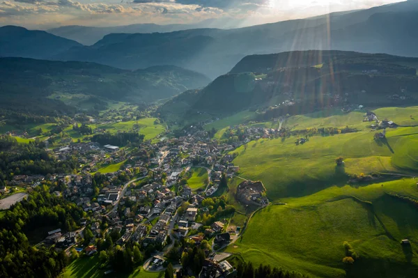 Aerial view of improbable green meadows of Italian Alps, green slopes of the mountains, Bolzano, huge clouds over a valley, roof tops of houses, Dolomites on background, sunshines through clouds — Stock Photo, Image