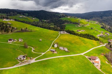 Olağandışı yeşil İtalyan Alpleri çayırları, dağların yeşil yamaçları, Bolzano, vadideki devasa bulutlar, evlerin çatıları, arka planda Dolomitler, bulutların arasından gün ışığı.