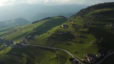Olağandışı yeşil İtalyan Alpleri çayırları, dağların yeşil yamaçları, Bolzano, vadideki devasa bulutlar, evlerin çatıları, arka planda Dolomitler, bulutların arasından gün ışığı.